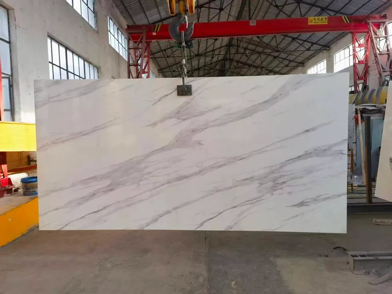 White slab with grey veining hanging from a clamp under a red gantry crane in a workshop